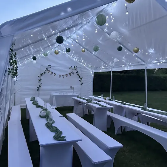 Festzelt in der Dämmerung mit Lichterketten, Lampions und weiß bezogenen Biertischen