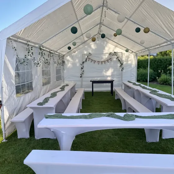 Blick in ein Festzelt mit weiß bezogenen Bierbänken und salbeigrünen Tischläufern
