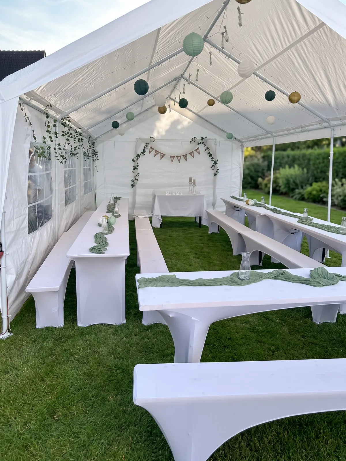Lange Tafeln aus Bierzeltgarnituren mit weißen Hussen, Glasvasen und grünen Läufern bei einer Hochzeit